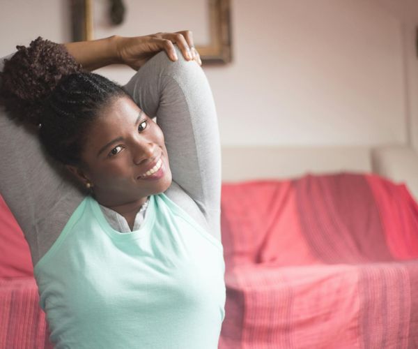 A person smiling while doing a simple stretching exercise at home.